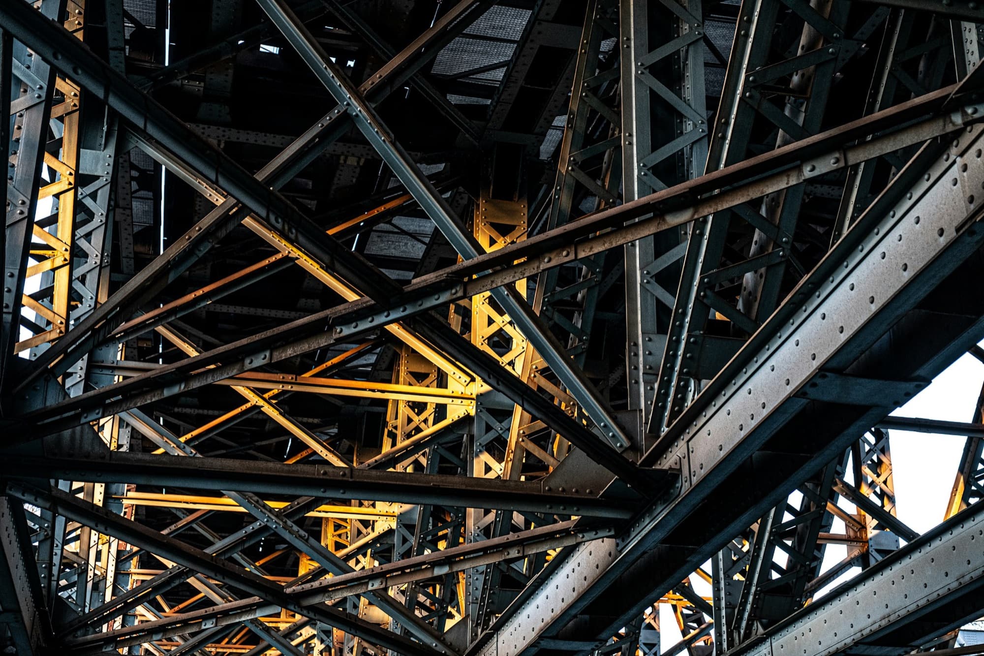 Stahlträger unter einer Brücke, dahinter warmes Licht